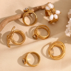 Close-up of gold snake head rings with pearls and zircons on warm silk background
