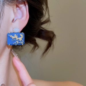 Close-up of rectangle enamel earrings featuring golden floral embossing and opal stone