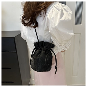 Rear view of a black drawstring bucket bag with pleated texture on a model's shoulder