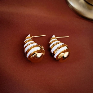 Macro view of gold-plated croissant earrings with white enamel stripes and glossy finish