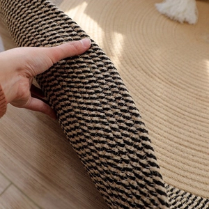 Handwoven jute rug with spiral texture and white fringe tassels on light wood floor
