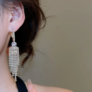 Close-up of long gold fringe earrings with sparkling rhinestones worn by a model