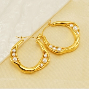 Detail of gold wavy earrings with embedded white pearls on a silk marble background