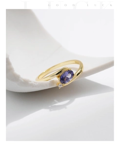 Macro side view of gold ring featuring an oval purple gemstone on white curved stand