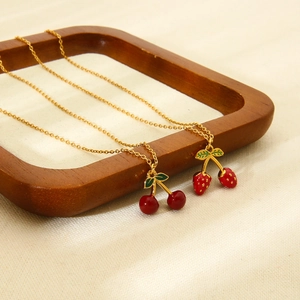 Detail shot of cherry and strawberry pendants on gold chains over a wooden tray