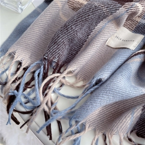 Detail of soft plaid scarf showing blue and beige patterns with tassel and label