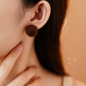Close-up of minimalist dark brown flocked round stud earring on model for elegant look