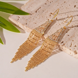 Détail de boucles d'oreilles pompons dorés avec triangle serti de zircons et franges