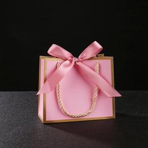 Pink gift bag with gold trim, ribbon bow, and woven handles on a black background