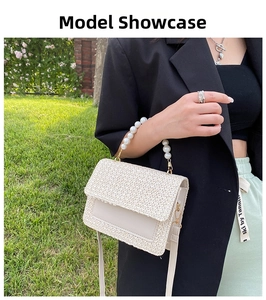 Detail of a beige woven handbag with pearl handle and detachable strap on a model