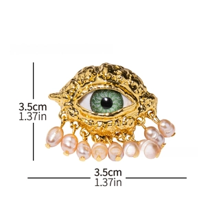 Detailed view of evil eye brooch in gold metal with green center and pink pearl tassels