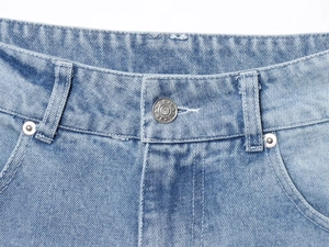Detailed macro view of denim waistband featuring a metallic button and rivets on light blue jeans