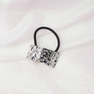 Detail shot of silver textured irregular metal plate on black elastic hair tie