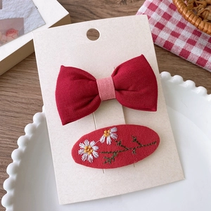 Détail de la barrette nœud rouge et des épingles à cheveux marguerites brodées