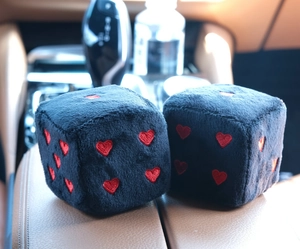 Close-up of black plush car dice hanging ornaments with red heart embroidery detail