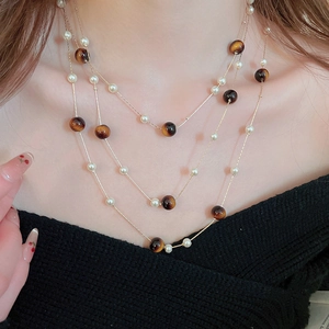 Gros plan d'un collier multicouche avec perles et œil de tigre sur un pull en maille