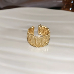 Macro detail of wide gold open ring featuring unique lava texture on wavy white plate