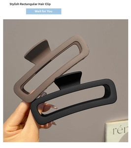 Detail showing hand holding two matte rectangle hair claws in coffee and black colors