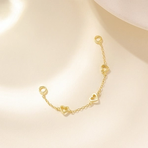 Detail of a golden chain accessory featuring hollow heart-shaped charms and secure clasps