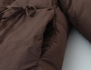 Detail of dark brown puffer jacket showing waist drawstring and side pocket stitching