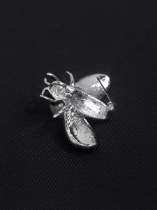 Macro shot of silver bee brooch showing wings texture and safety pin clasp