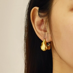 Detail of gold twisted rope earrings with irregular crumpled texture on a model's ear