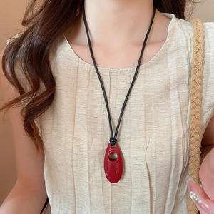 Detail of red geometric oval resin pendant on a black cord worn by a model