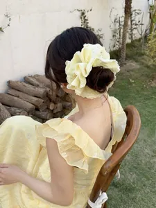 Detailed view of yellow lace floral scrunchie with embroidery on a model in a garden