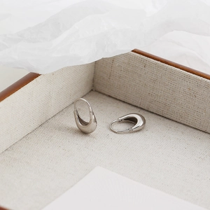 Close-up of minimalist silver water drop hoop earrings on a linen texture tray