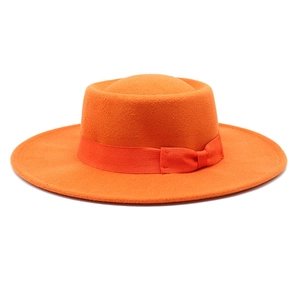 Detail of an orange wool felt boater hat featuring a matching grosgrain ribbon and bow