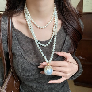 Detail of a multi-layer pearl necklace with a large pendant on a knitted sweater