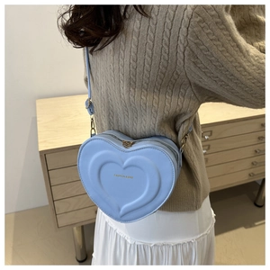Detail of light blue heart-shaped leather crossbody bag with embossed patterns shown on model