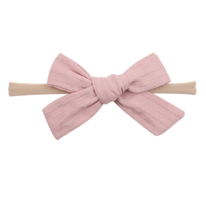 Detail shot of a soft pink dotted fabric bow attached to a beige elastic nylon headband