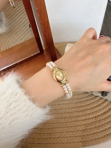 Detail of vintage gold oval watch with double-strand pearl bracelet on a wrist