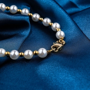 Elegant stainless steel pearl bracelet with gold spacer beads on blue silk background