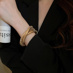 Macro detail of layered gold spiral bracelet on a black suit sleeve for a luxury look