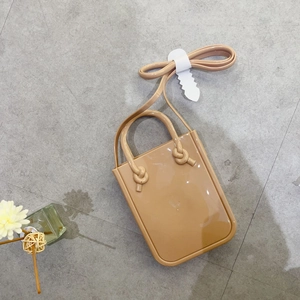 Mini beige PVC jelly handbag with dual handles and long shoulder strap on grey floor