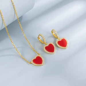 Macro shot of gold heart necklace and earrings set with red gems and zircon borders