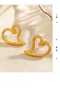 Detail view of gold hollow heart stud earrings on elegant beige silk fabric background