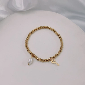Close-up of golden beaded bracelet with pearl drop and heart key charm on white silk