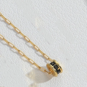 Macro d'un collier doré avec pendentif circulaire en zircon noir sur cuir blanc