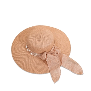 Detail of khaki wide brim straw hat featuring elegant ribbon bow, pearls, and floral accents