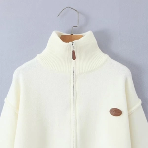 White zip-up knit cardigan with high collar and decorative leather patch on a wooden hanger
