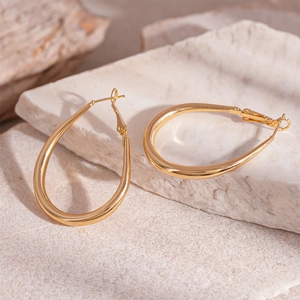 Macro detail of polished gold teardrop hoop earrings resting on a natural stone base