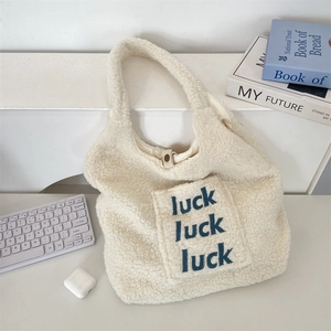 Close-up of fluffy white faux fur tote bag featuring embroidered luck luck luck lettering