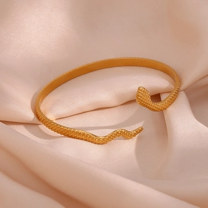 Macro detail of gold snake-shaped open cuff bracelet with textured scale finish