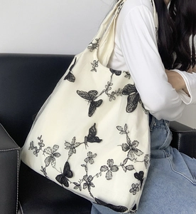 Dettaglio borsa tote in tela bianca con eleganti ricami di farfalle nere e pizzo floreale