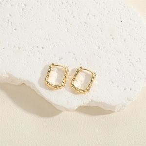 Golden square hoop earrings with molten texture on white stone and beige backdrop