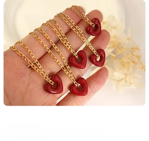 Close-up of elegant gold necklaces with red heart pendants held in hand over white decor