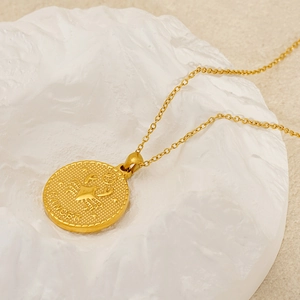 Detailed macro view of 18k gold Cancer zodiac pendant on white textured stone background